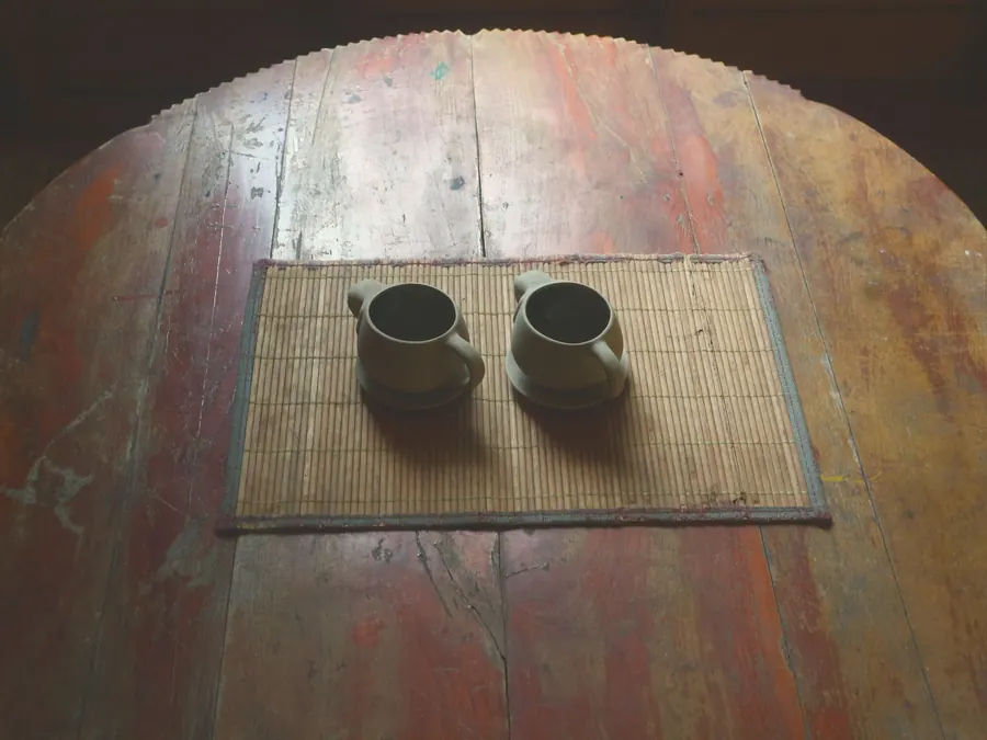 Two cups on a woven mat on a teak table